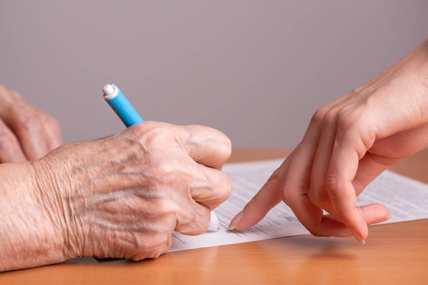 Elderly woman signs a paper document. Signing papers. An elderly man signs a document. - Foto, imagen