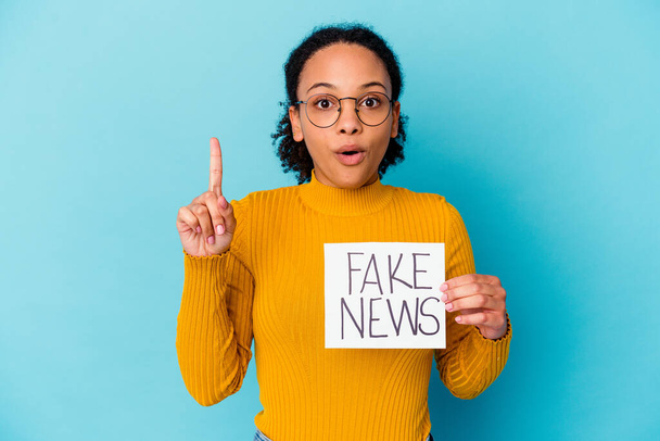 Young african american mixed race woman holding a fake news concept having an idea, inspiration concept. - Photo, Image
