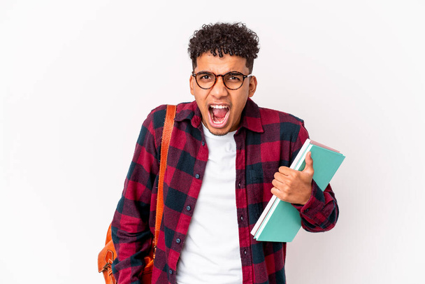 Young african american student curly man isolated holding books screaming very angry and aggressive. - 写真・画像