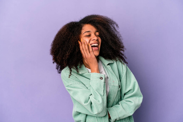Junge afrikanisch-amerikanische lockige Frau auf lila Hintergrund isoliert lacht glücklich und hat Spaß, die Hände auf dem Bauch zu halten. - Foto, Bild