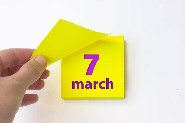 7 марта. день 7 месяца, календарная дата. Рука отрывает желтый лист календаря. Концепция "весенний месяц, день года" - Фото, изображение