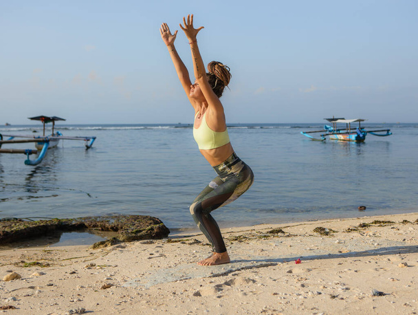 Λευκή γυναίκα προπονείται στο Ουτκατασάνα, στην καρέκλα Πόουζ. Χαμηλά κατάληψη asana σε hatha γιόγκα. Ψηλά τα χέρια. Ισορροπία και συγκέντρωση. Yoga καταφύγιο. Thomas beach, Μπαλί, Ινδονησία - Φωτογραφία, εικόνα