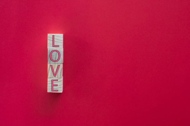 Take a close-up shot. The "LOVE" letters on the wooden cube are arranged vertically on a red background. Concept of Love Day or Valentine Day - Foto, imagen