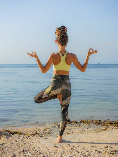 Jeune femme pratiquant Vrikshasana, Pose d'arbre sur la plage. Mains dans le mudra gyan. Équilibre et concentration. Retraite de yoga. Concept de soins de santé. Vue de dos. Plage Thomas, Bali, Indonésie - Photo, image