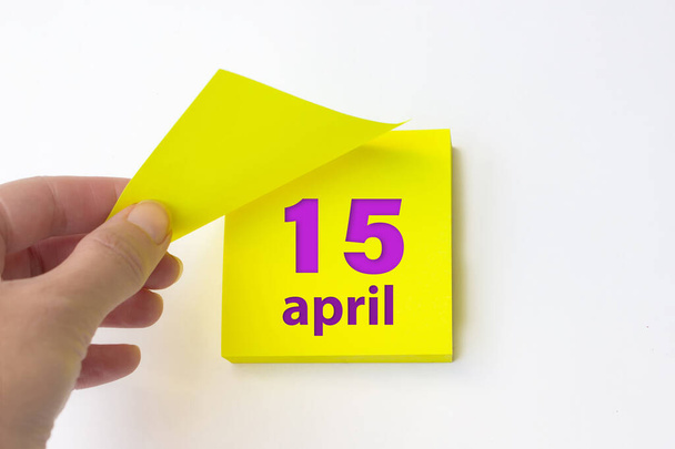 15 апреля. 15 апреля. день 15 месяца, календарная дата. Рука отрывает желтый лист календаря. Концепция "весенний месяц, день года" - Фото, изображение