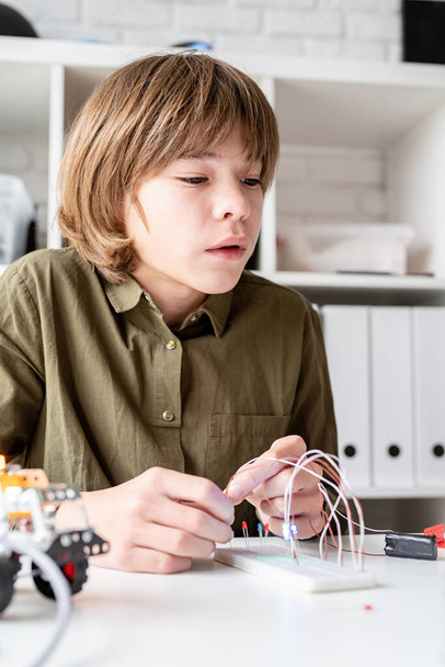 12 éves fiú robotautót épít az asztalnál ülve. - Fotó, kép