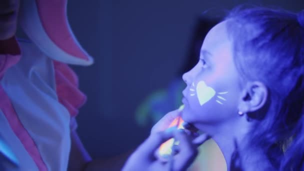 Animator rysuje neonowe serce za pomocą makijażu na policzku dziewczyny - Materiał filmowy, wideo