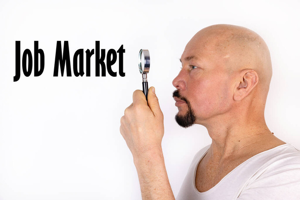 An American man looks through a magnifying glass at the word, text Job Market. Business concept. - 写真・画像
