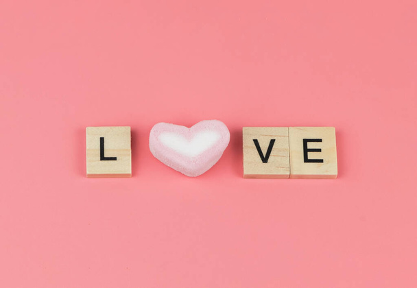Bovenaanzicht van het woord LOVE van houten letter en hart vorm marshmallow op roze achtergrond. - Foto, afbeelding