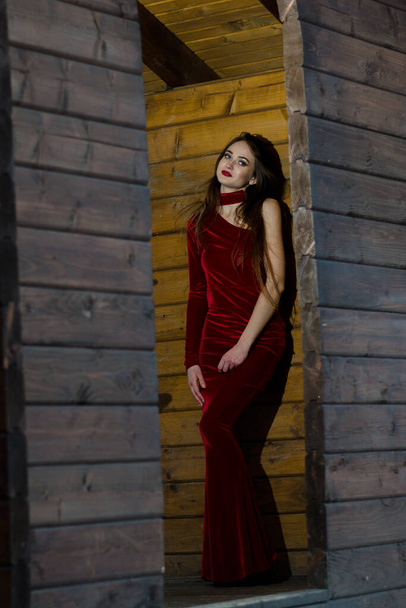 Retrato vertical de belleza. La imagen de una señora sensual, cuerpo elevado y tonificado, en un vestido rojo posa en una habitación de madera. - Foto, Imagen