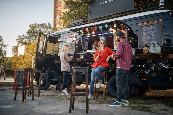 young couple flirting in front of truck with food while employee looking at them - Foto, imagen