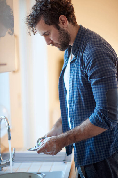 Single Caucasian man washing the dishes in the kitchen - Fotó, kép