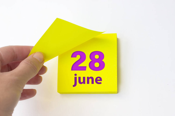 28 de junio. Día 28 del mes, fecha del calendario. La mano arranca la hoja amarilla del calendario. Mes de verano, concepto del día del año - Foto, Imagen