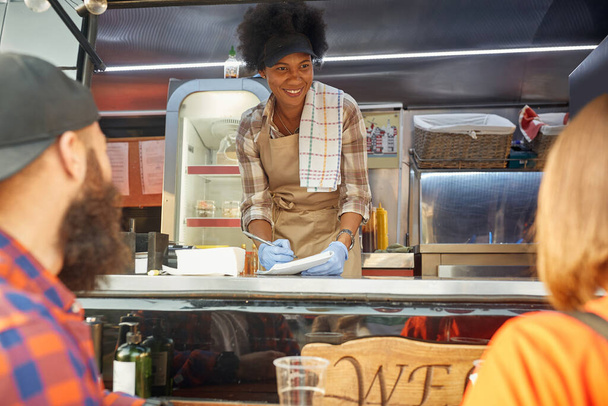young urban couple ordering food to female afro-american employee in food-truck  - Foto, imagen