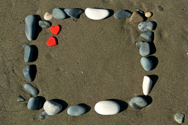 Vierkant frame van stenen op strand zand met twee kleine rode harten  - Foto, afbeelding