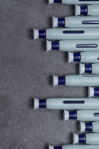 Layout graphic of a row of syringe self application pens against a rustic textured gray background. - Фото, изображение