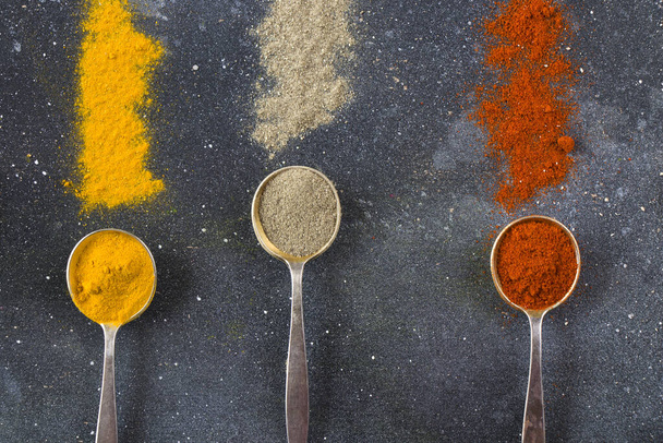 A top view closeup of the variety of spices on the vintage silver spoons on a blue background - 写真・画像