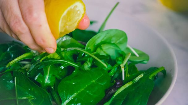 A selective focus of a hand squeezing lemon on a fresh spinach salad - Foto, Imagem