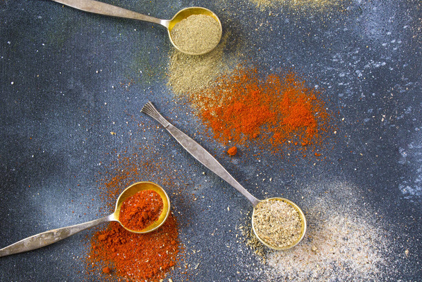 A top view closeup of the variety of spices on the vintage silver spoons on a blue background - Photo, image