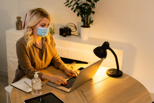 Ofiste. Yüz maskeli kadın, dezenfektan masanın yanında duruyor. - Fotoğraf, Görsel