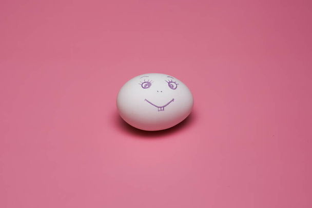 chicken egg with painted face smiling emoticon on a pink background. Easter. - Fotó, kép