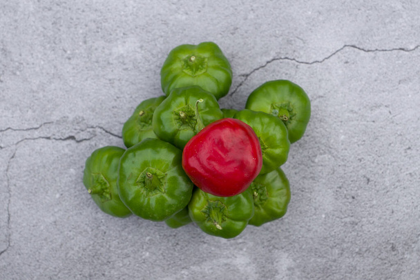A top view of red bell pepper on a pile of green bell peppers on a cracked concrete surface - Фото, изображение