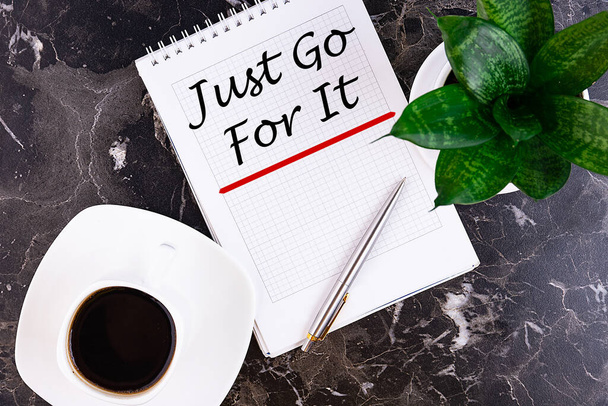 Just Go For It motivational message is written in a notebook lying on a grey table with a pen and a cup of coffee. Business concept - Фото, изображение