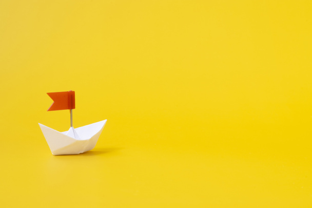Barco de papel blanco con bandera roja sobre fondo amarillo. El concepto de éxito y desarrollo. Negocio. - Foto, imagen