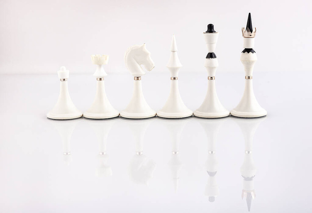 White chess pieces on a reflective surface. Business concept. Game, strategy, wisdom, determination. - Zdjęcie, obraz