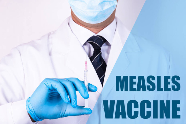 麻疹ワクチンのテキストは、医療用マスクと手袋でワクチンで注射器を保持している医師の背景に書かれています。医学的概念. - 写真・画像