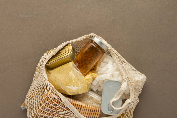 Home food supplies, necessary food for the period of quarantine and isolation, the concept of stay at home, eco bag with pasta and rice, canned food and cookies, sugar and honey, top view - Photo, Image