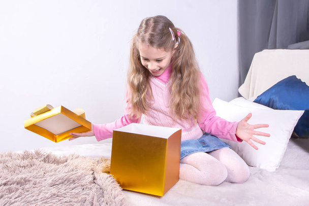 Cute birthday girl opening boxes with presents while sitting on bed at home. Concept happy gift - Photo, Image
