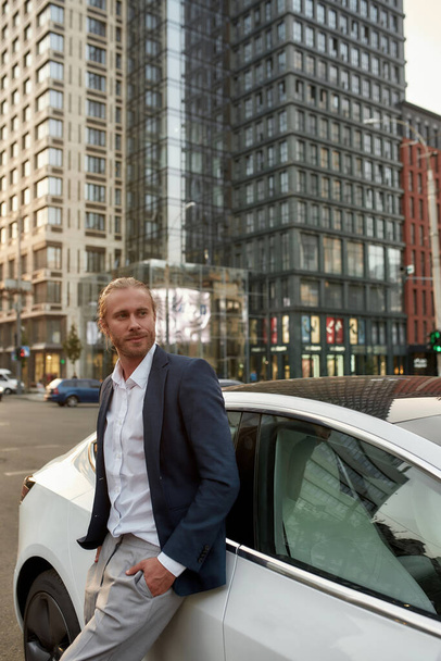 Smiling young businessman standing near white car - Foto, Bild