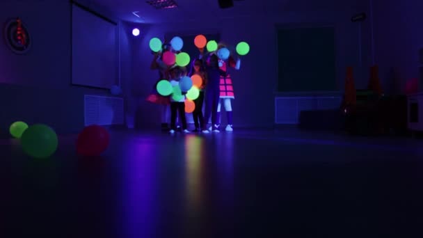 Célébration d'anniversaire - petits enfants et animateurs tenant et vomissant des ballons dans l'éclairage au néon - Séquence, vidéo