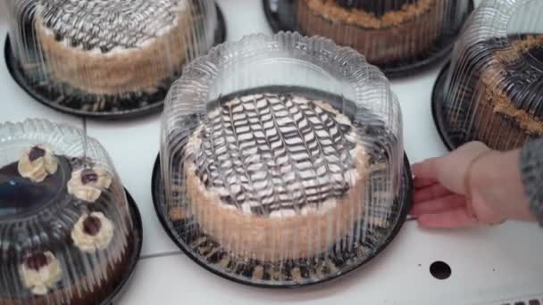 Escaparate con deliciosos pasteles envasados en envases de plástico transparente en un primer plano de supermercado. Mujer mano toma una caja con postre - Metraje, vídeo