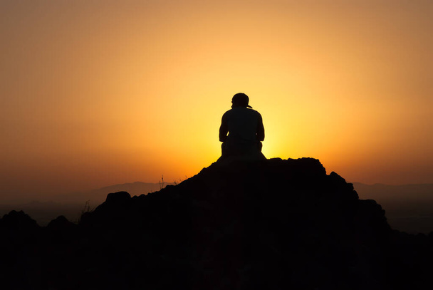 silhouette d'un homme sur la montagne regardant le coucher de soleil assis - Photo, image