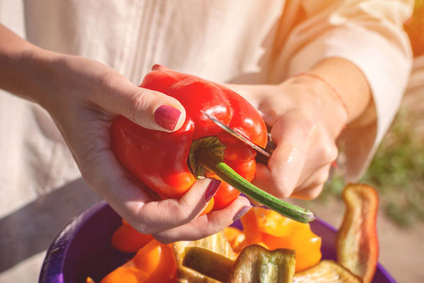 Woman's hand cuts ripe red peppers. Cutting Bell Pepper outdoors. Cooking fresh, ripe, bell pepper salad during a picnic. Summer fresh vegetable salad. - Foto, Imagem