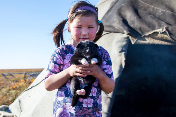 Ένα νεαρό κορίτσι, με τα εθνικά χειμωνιάτικα ρούχα των βόρειων κατοίκων της τούνδρας, παίζει με ένα σκύλο - Φωτογραφία, εικόνα