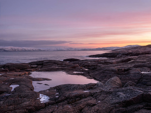 Cudowny górski krajobraz z przylądkiem na brzegu morza Barentsa. Niesamowity krajobraz wschodu słońca z polarnym białym śnieżnym pasmem gór. - Zdjęcie, obraz