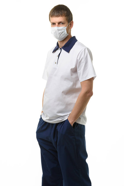 Portrait d'un médecin dans un masque médical sur fond blanc, le médecin a mis ses mains dans ses poches - Photo, image
