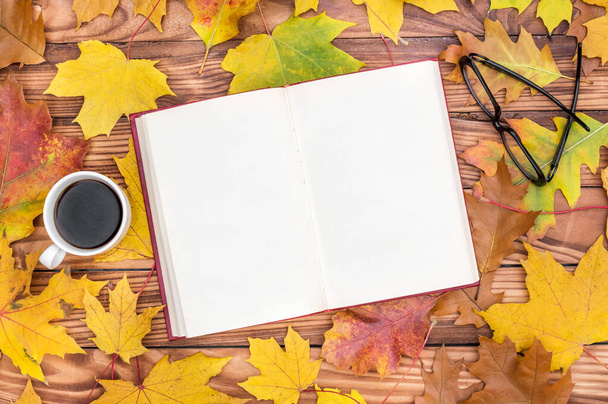 Opened blank book with cup of coffee and eyeglasses on the table with autumn leaves. - Foto, Imagen