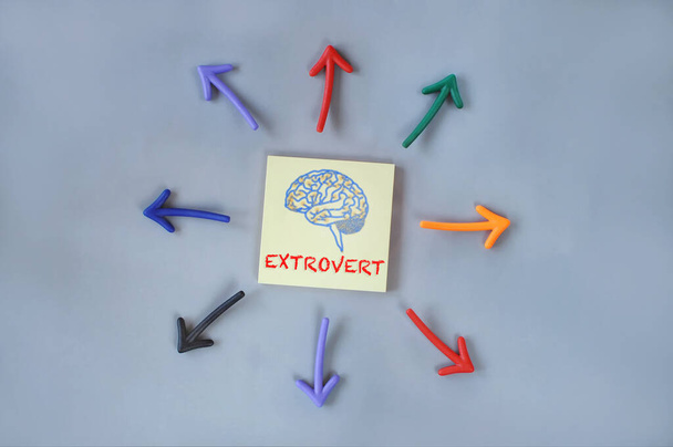 Extrovertido y cerebro escrito en nota adhesiva amarilla y flecha colorida sobre fondo gris. Concepto de persona saliente e idea de personalidad - Foto, imagen