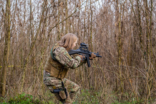 Gyönyörű lány katonai egyenruhában, légpuskával az erdőben. - Fotó, kép