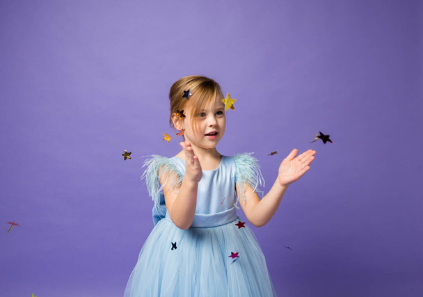 retrato de una niña pequeña y hermosa atrapando confeti volador sobre un fondo púrpura con espacio para el texto - Foto, imagen