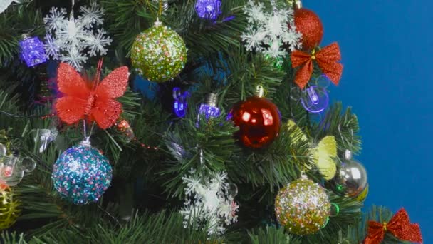 Σε μπλε φόντο, ένα χριστουγεννιάτικο δέντρο διακοσμημένο με διάφορα και πολύχρωμα παιχνίδια - Πλάνα, βίντεο