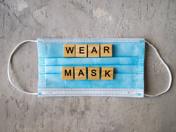 Words WEAR MASK lined with wooden letters on a background of blue surgical mask. - Фото, изображение