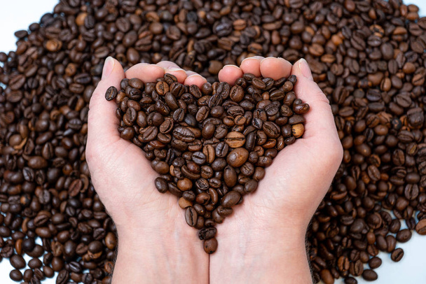 Kaffeebohnen in Großaufnahme auf der Handfläche in Herzform vor dem Hintergrund anderer Kaffeebohnen - Foto, Bild