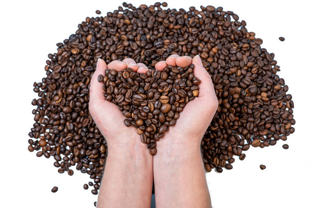 Kaffeebohnen in Großaufnahme auf der Handfläche in Herzform vor dem Hintergrund anderer Kaffeebohnen - Foto, Bild