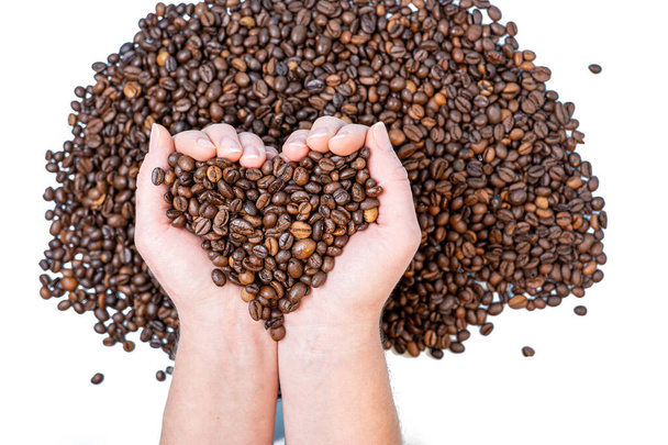 chicchi di caffè primo piano sulla palma a forma di cuore sullo sfondo di altri chicchi di caffè - Foto, immagini