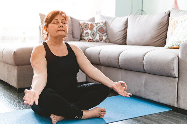 Middle aged woman in yoga position keeps fit in her home - Elderly person has fun doing sports - mental and physical well-being concept - warm filter on the background. - Foto, Imagem